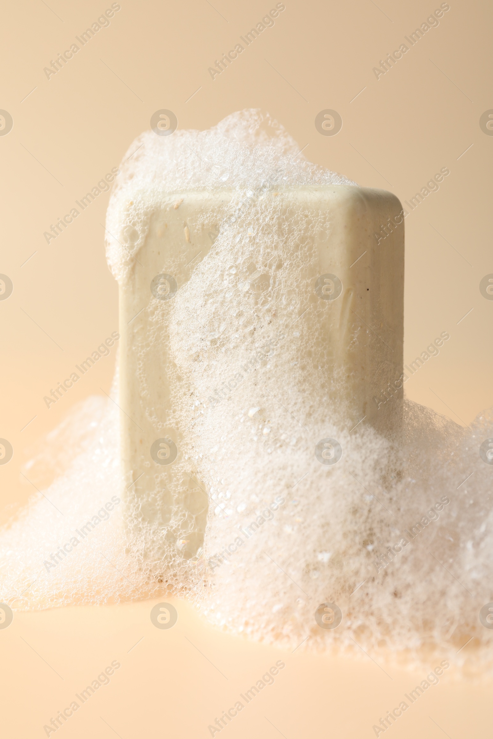 Photo of Soap bar with foam on beige background, closeup