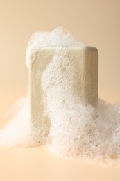 Photo of Soap bar with foam on beige background, closeup