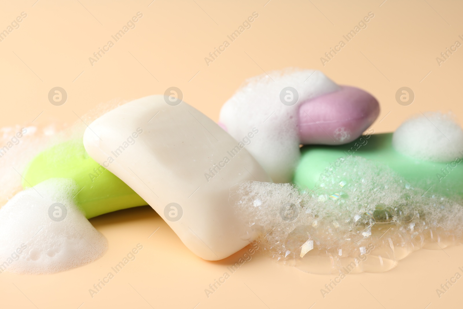 Photo of Soap bars with foam on beige background, closeup