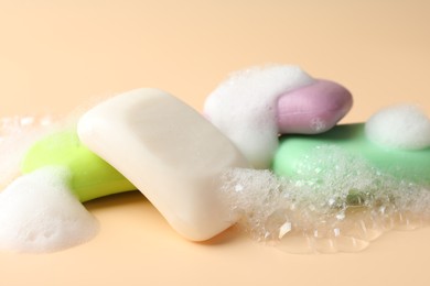 Photo of Soap bars with foam on beige background, closeup