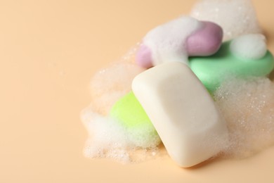 Photo of Soap bars with foam on beige background, closeup. Space for text