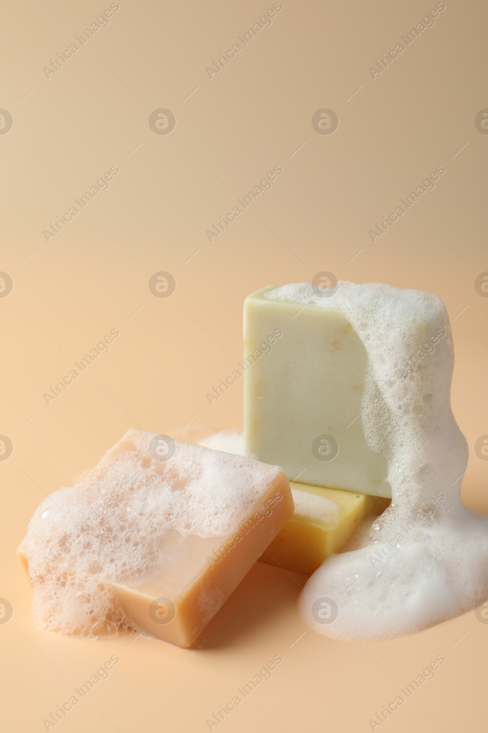 Photo of Soap bars with foam on beige background, closeup. Space for text