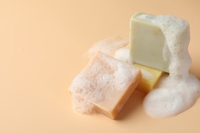 Photo of Soap bars with foam on beige background, closeup. Space for text