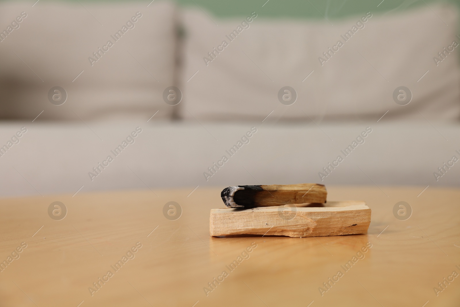 Photo of Burnt palo santo stick on wooden table indoors, space for text