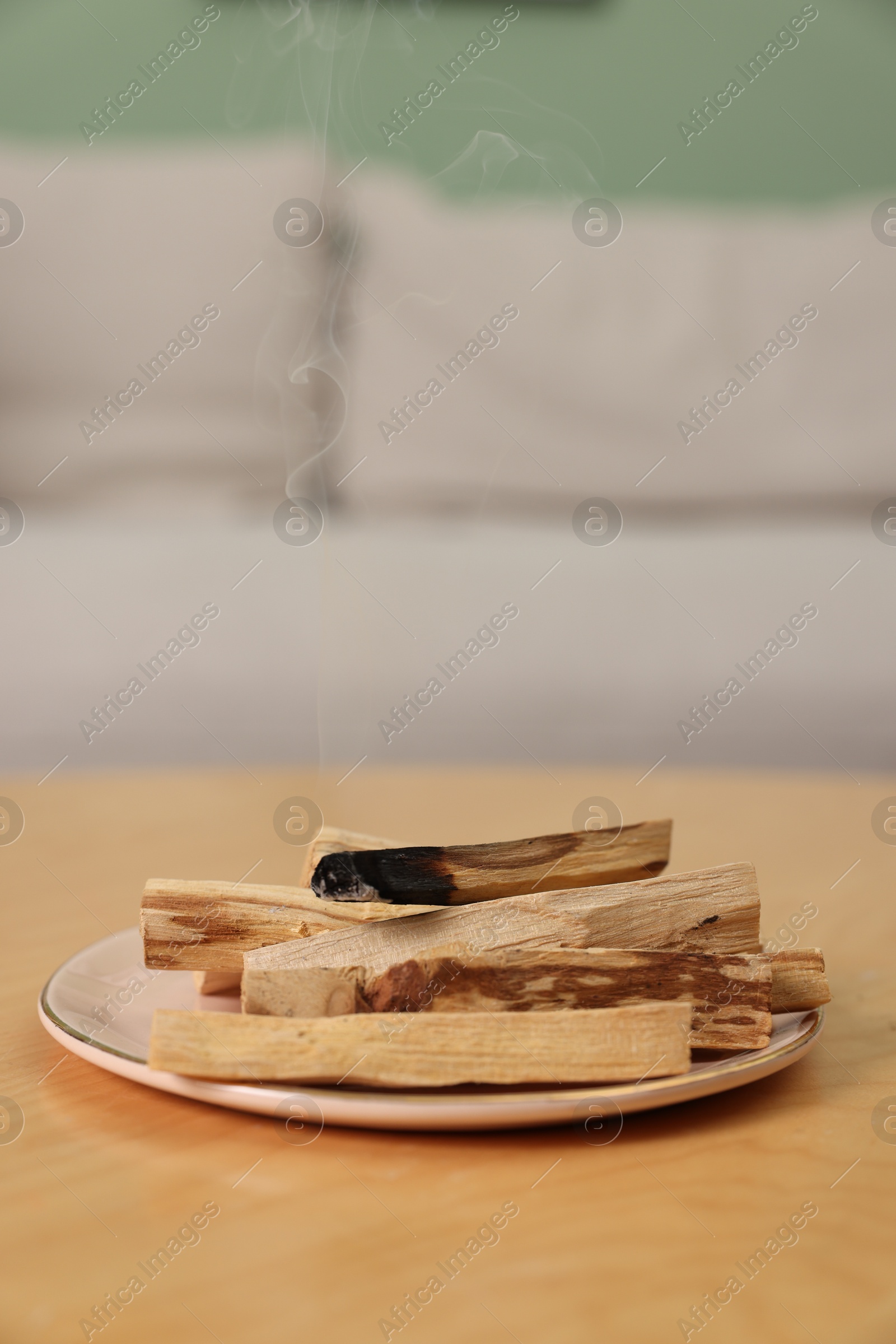 Photo of Palo santo sticks and smoldering one on wooden table indoors, space for text