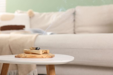 Photo of Palo santo sticks and smoldering one on white table indoors, space for text