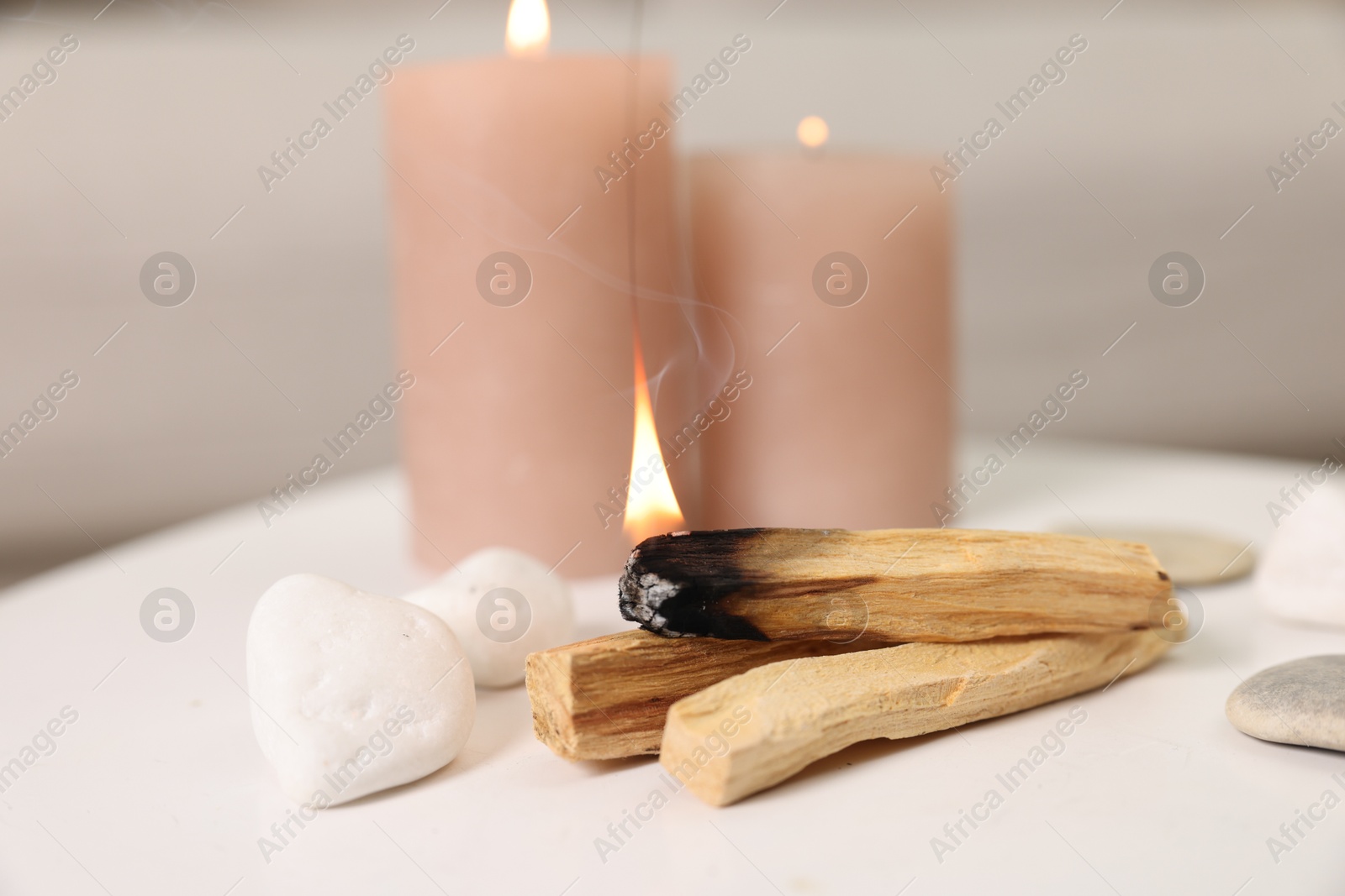 Photo of Palo santo sticks, burning candles and stones on white table indoors, closeup