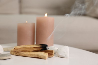 Photo of Palo santo sticks, burning candles and stones on white table indoors, space for text