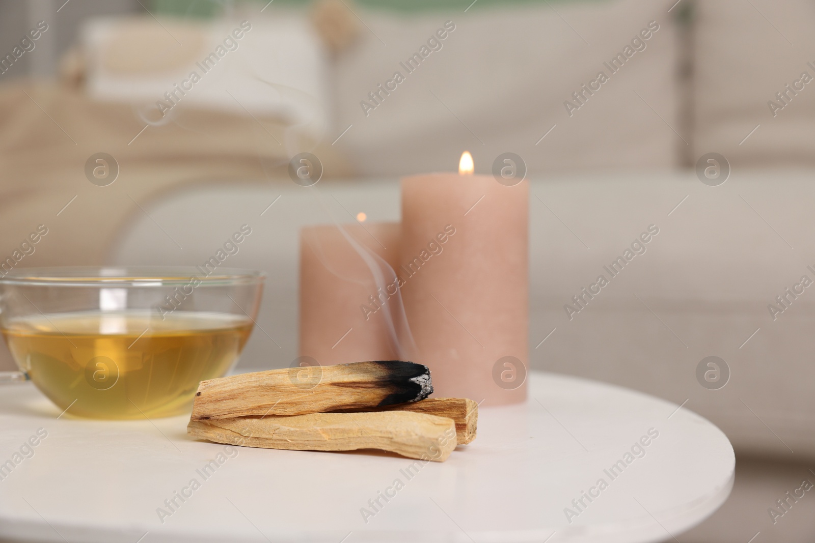 Photo of Palo santo sticks, burning candles and tea on white table indoors, space for text