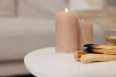 Photo of Palo santo sticks and burning candles on white table indoors, space for text