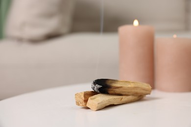 Photo of Palo santo sticks and burning candles on white table indoors, space for text