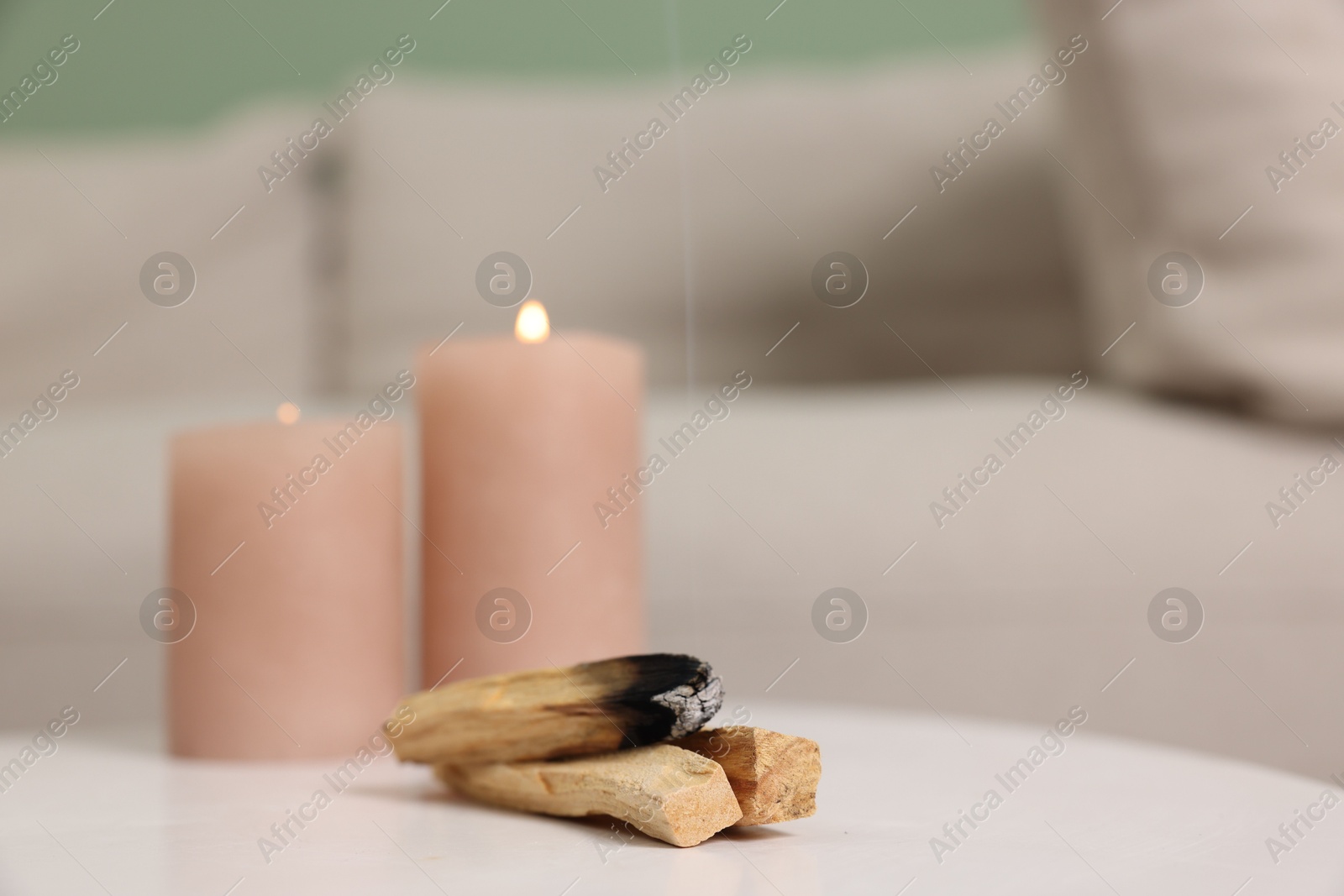 Photo of Palo santo sticks and burning candles on white table indoors, space for text