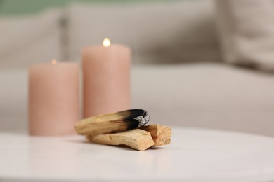 Photo of Palo santo sticks and burning candles on white table indoors, space for text