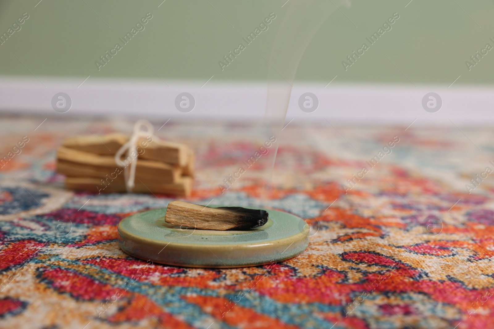 Photo of Smoldering palo santo stick on rug indoors