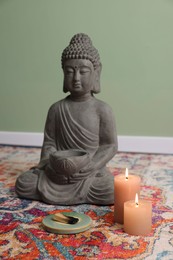 Photo of Buddha statue with palo santo sticks and burning candles on rug indoors