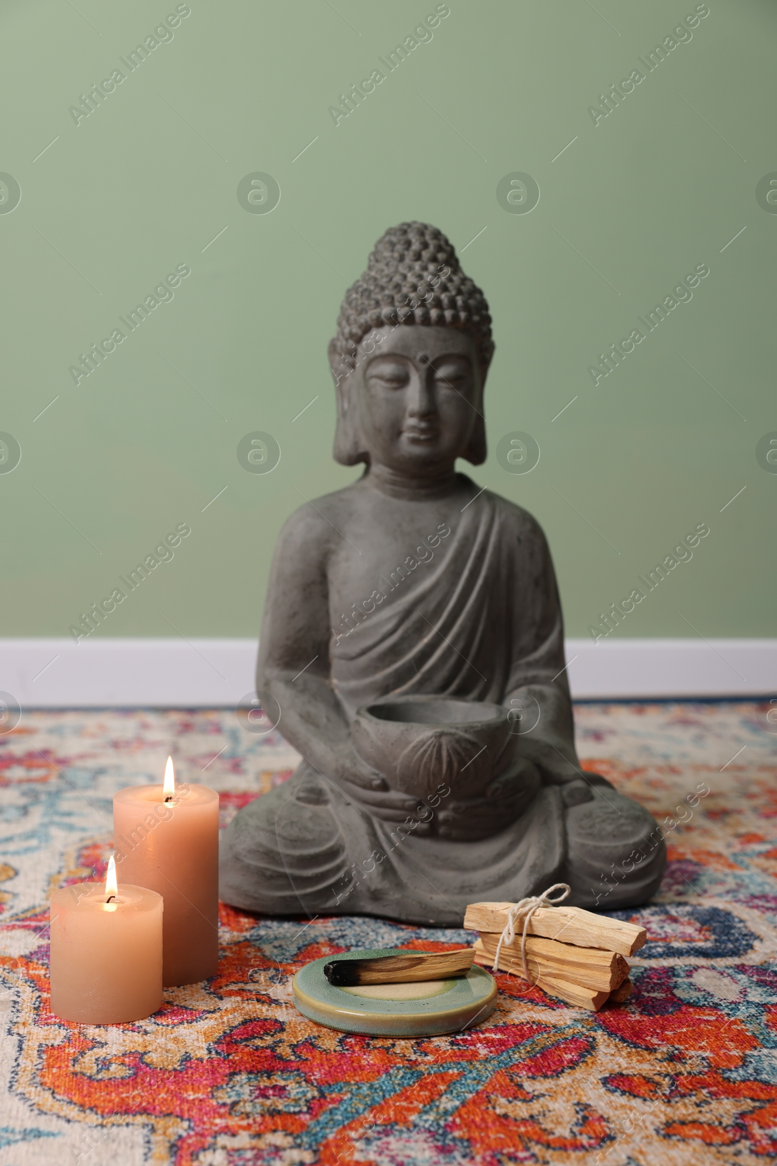 Photo of Buddha statue with palo santo sticks and burning candles on rug indoors