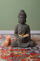 Photo of Buddha statue with palo santo sticks and burning candles on rug indoors