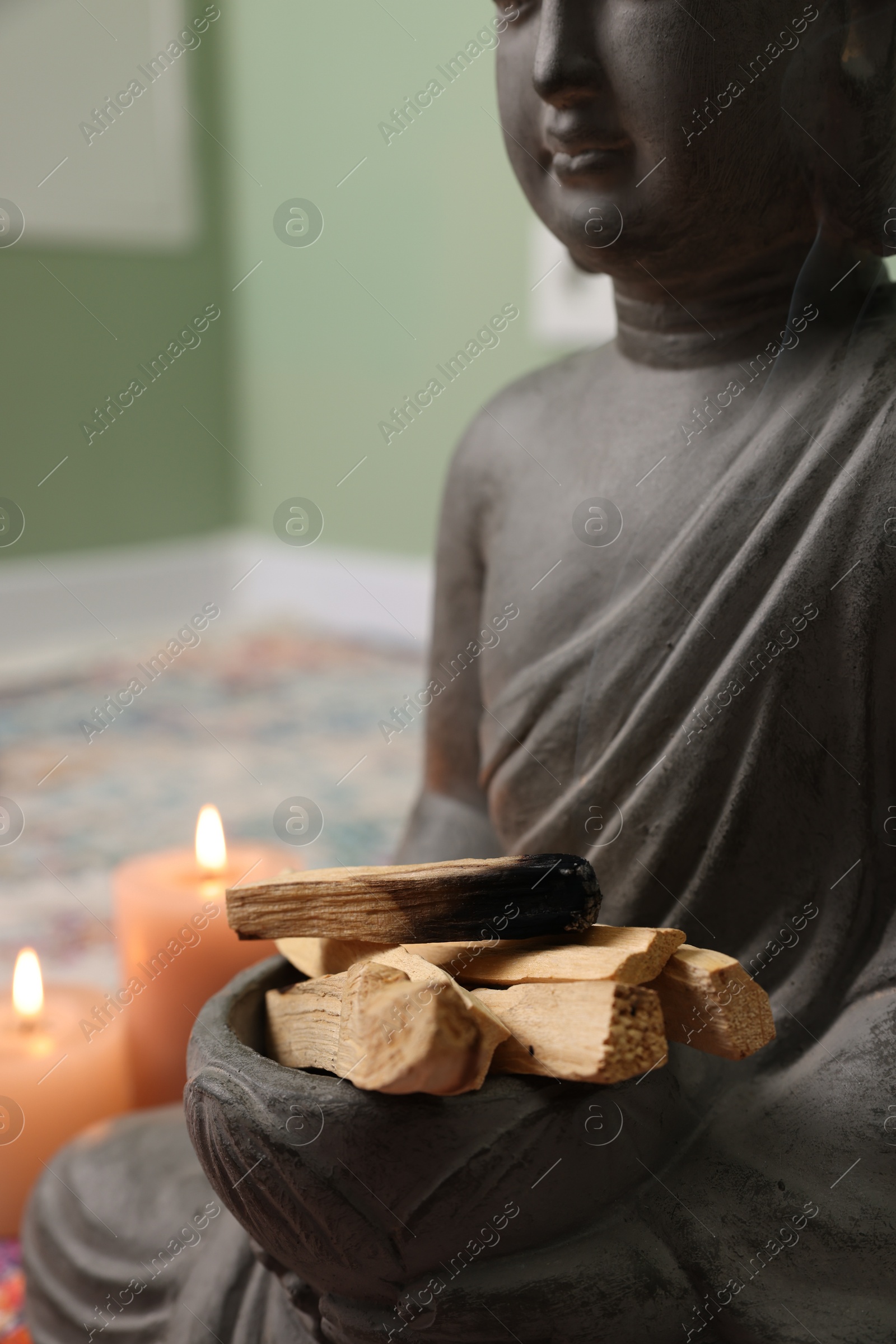 Photo of Buddha statue with palo santo sticks indoors, closeup