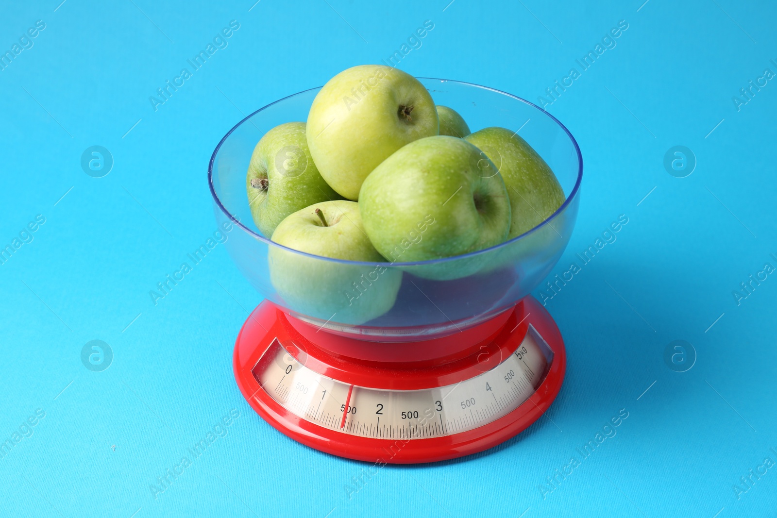 Photo of Kitchen scale with apples on light blue background, closeup