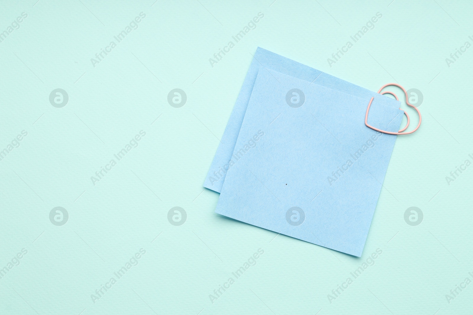 Photo of Paper notes attached with clip on light blue background, top view. Space for text