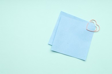 Photo of Paper notes attached with clip on light blue background, top view. Space for text