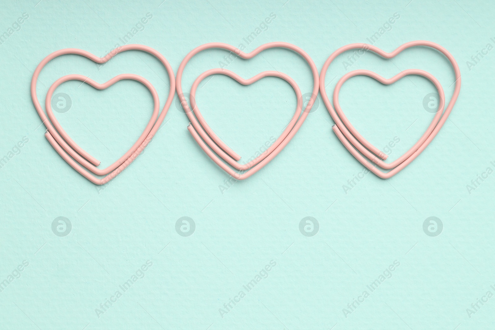 Photo of Heart shaped paper clips on light blue background, flat lay