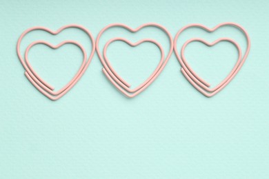 Photo of Heart shaped paper clips on light blue background, flat lay