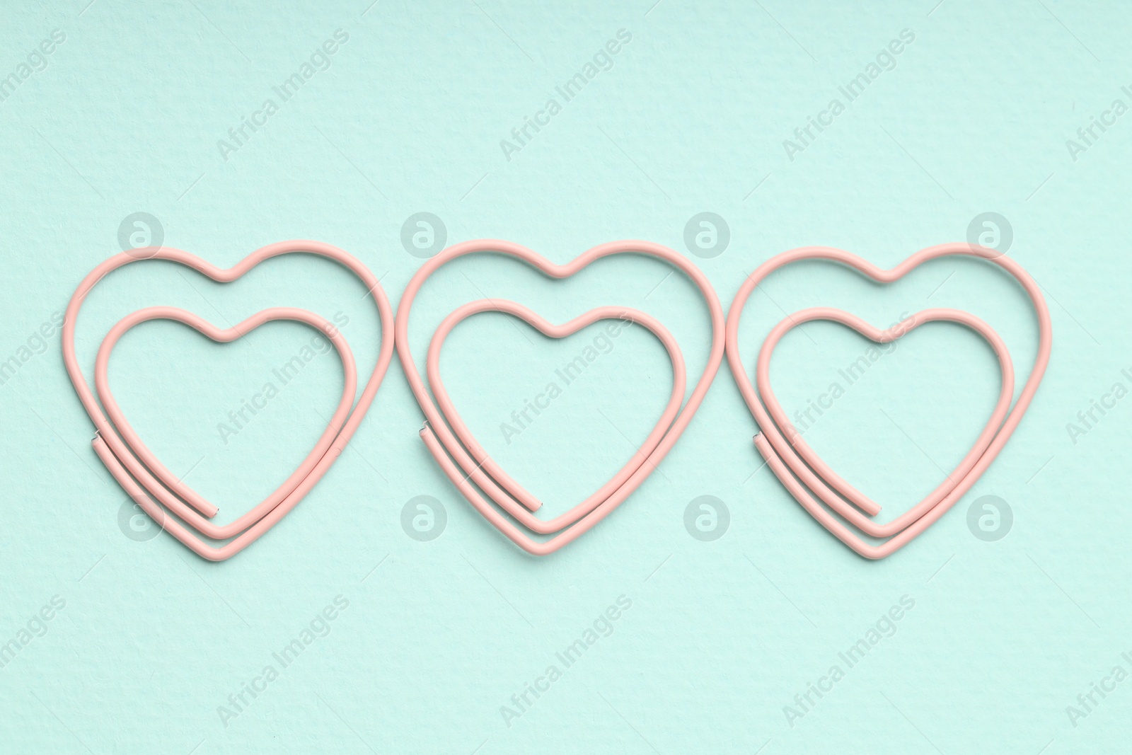 Photo of Heart shaped paper clips on light blue background, flat lay