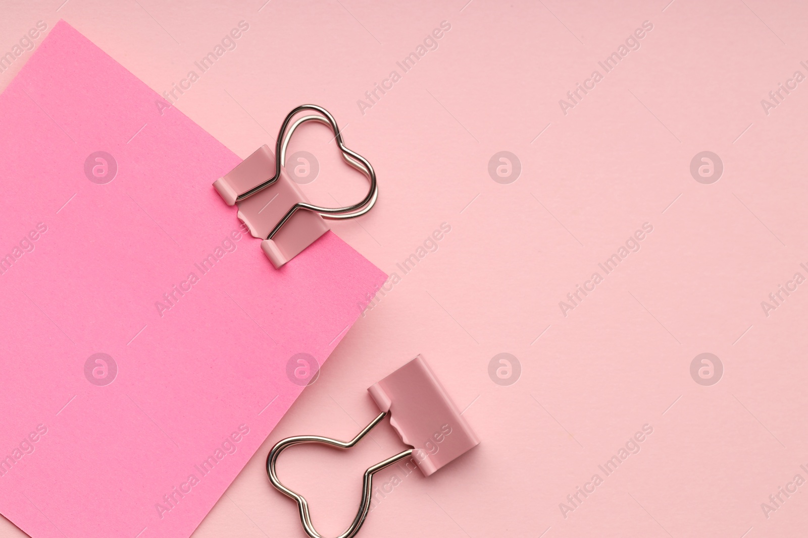 Photo of Heart shaped binder clips and blank paper note on pink background, flat lay. Space for text