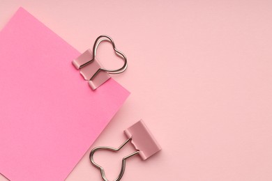 Photo of Heart shaped binder clips and blank paper note on pink background, flat lay. Space for text