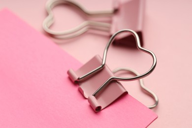 Photo of Paper note attached with binder clip on pink background, closeup