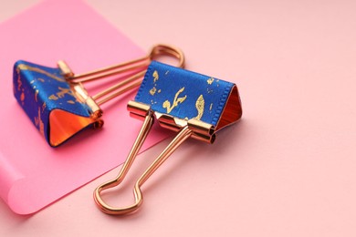 Photo of Binder clips and paper note on pink background, closeup. Space for text