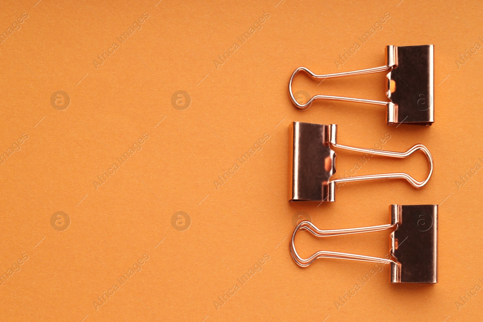 Photo of Golden binder clips on orange background, flat lay. Space for text