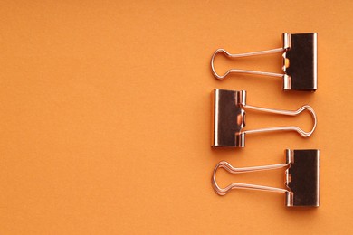 Photo of Golden binder clips on orange background, flat lay. Space for text