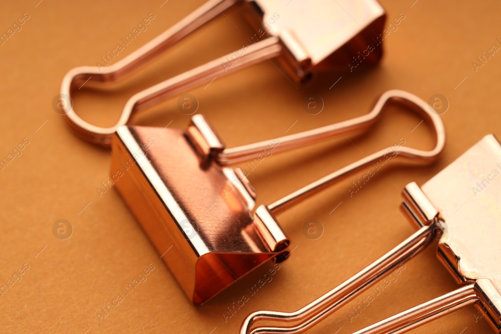 Photo of Golden binder clips on orange background, closeup