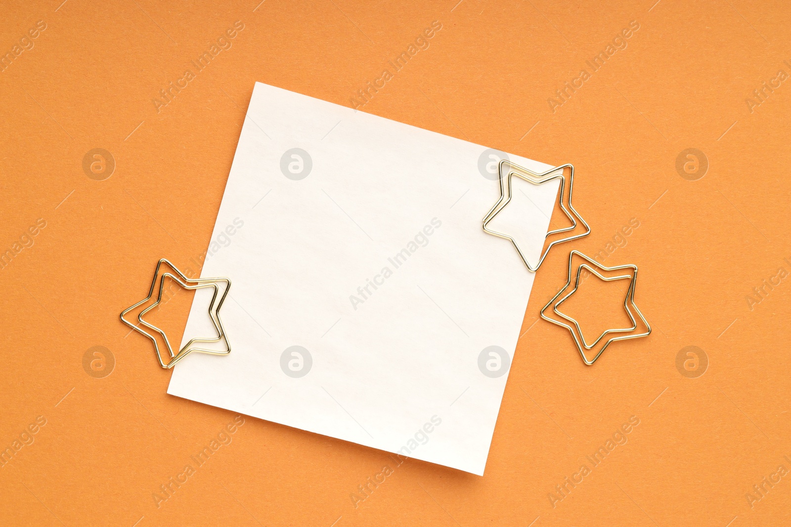 Photo of Star shaped clips and blank paper note on orange background, flat lay