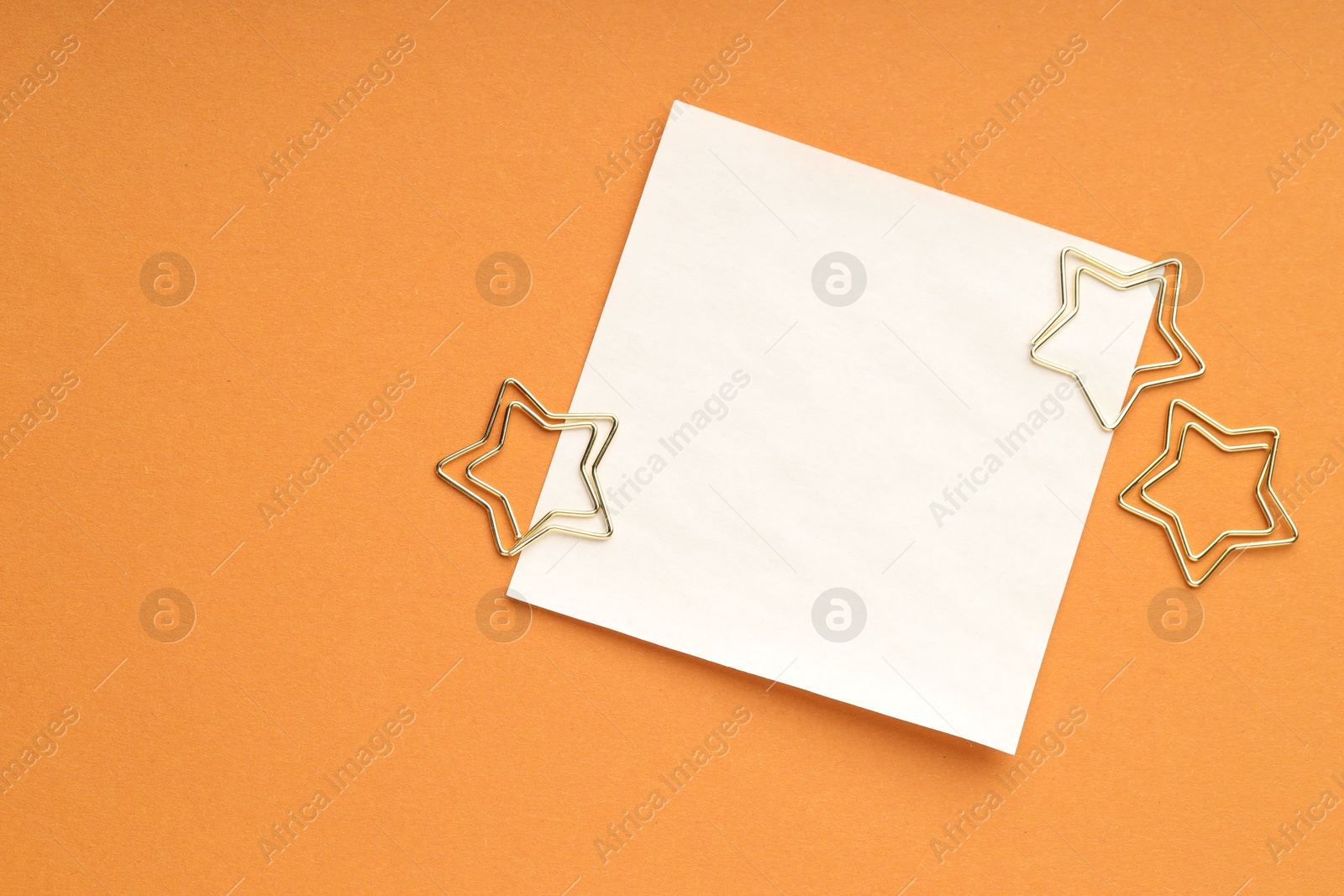 Photo of Star shaped clips and blank paper note on orange background, flat lay. Space for text