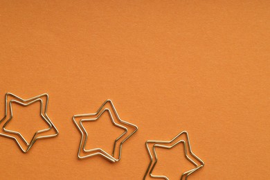 Photo of Star shaped paper clips on orange background, flat lay. Space for text