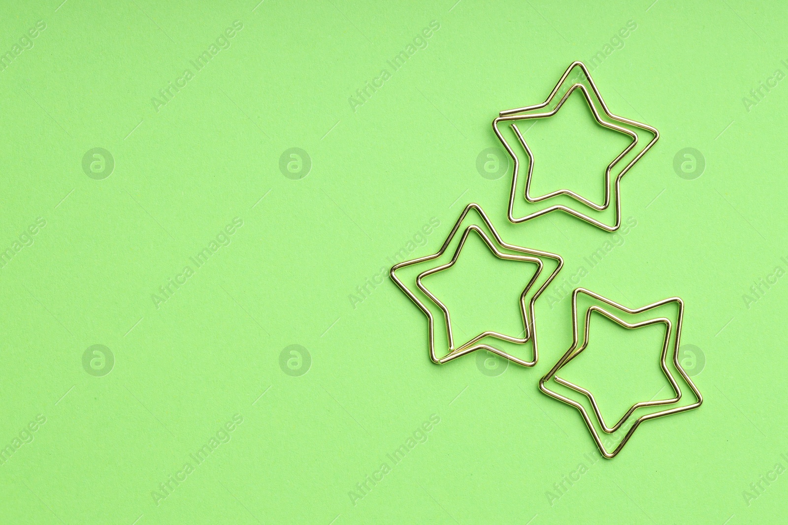 Photo of Star shaped paper clips on green background, flat lay. Space for text