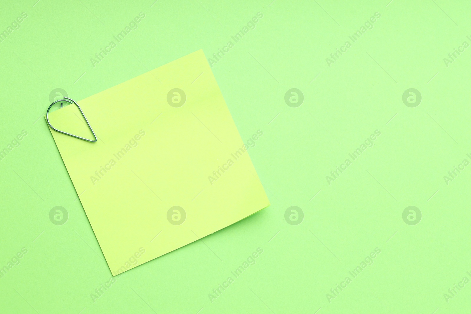 Photo of Blank paper note attached with clip on green background, top view. Space for text