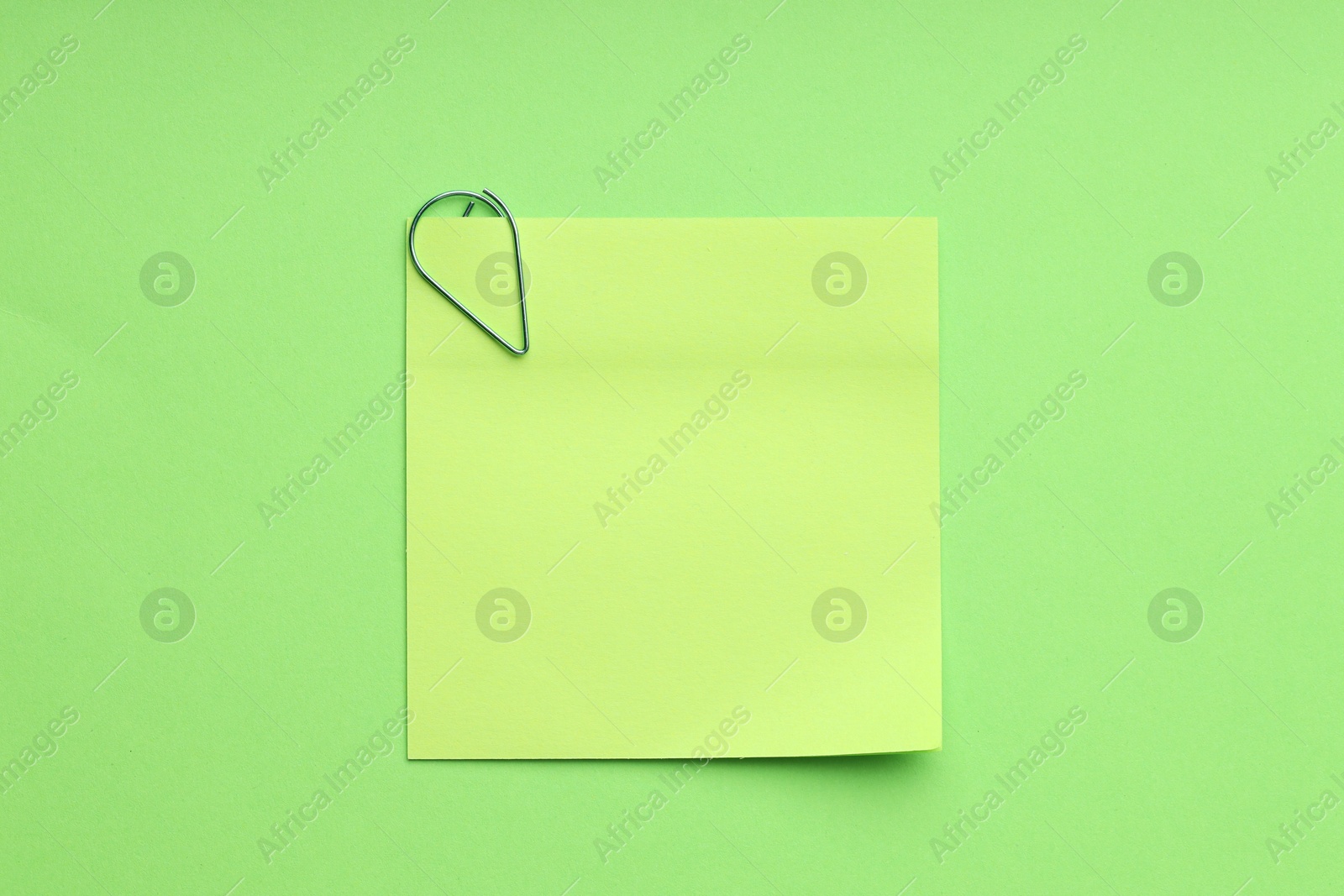 Photo of Blank paper note attached with clip on green background, top view