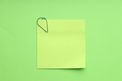 Photo of Blank paper note attached with clip on green background, top view