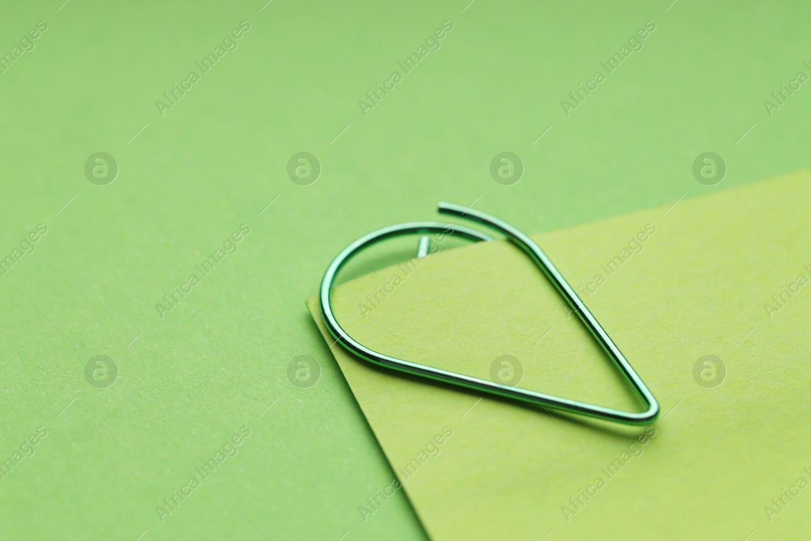 Photo of Paper note attached with clip on green background, closeup. Space for text