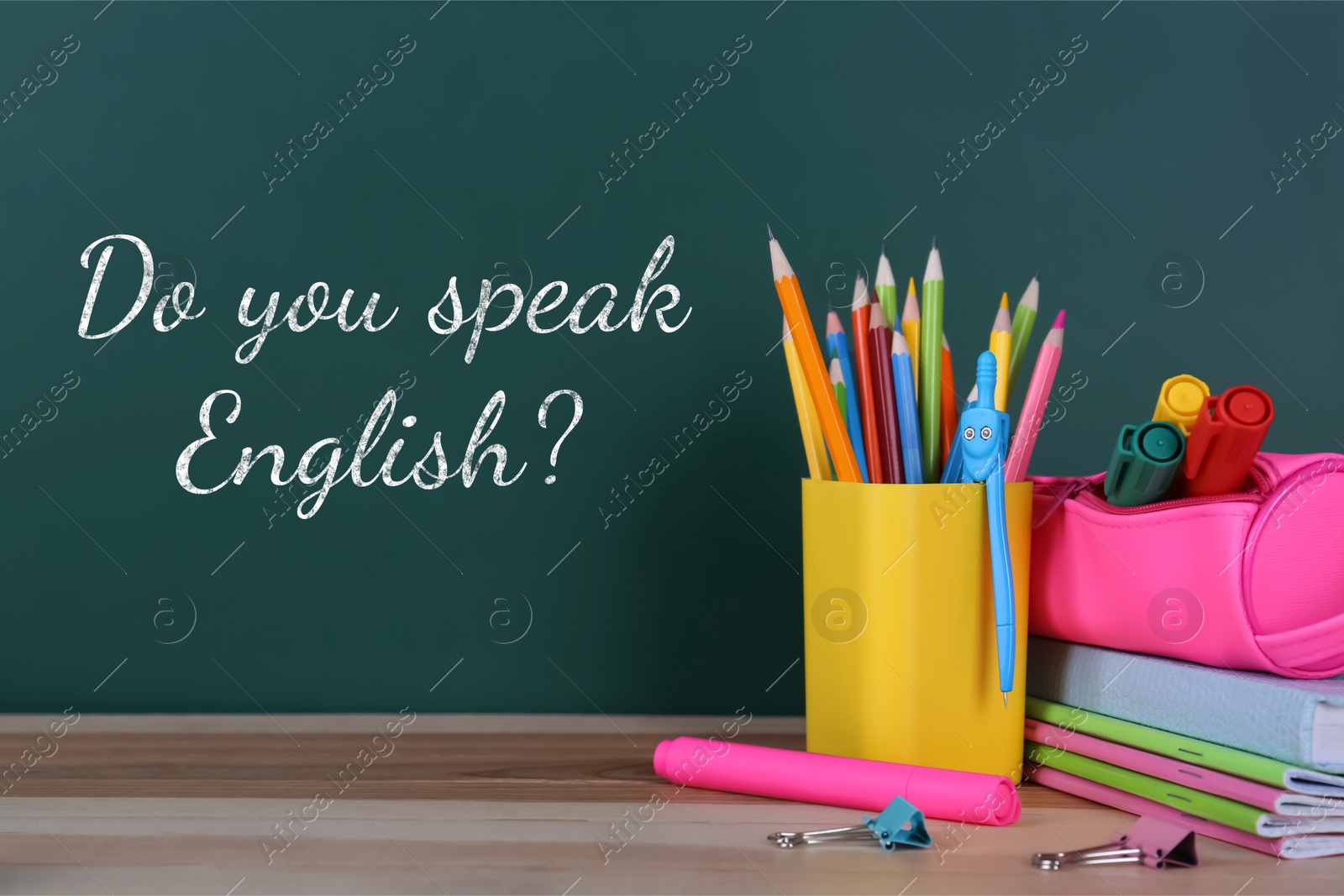 Image of Do You Speak English? text on green chalkboard and stationery on wooden table. Language course