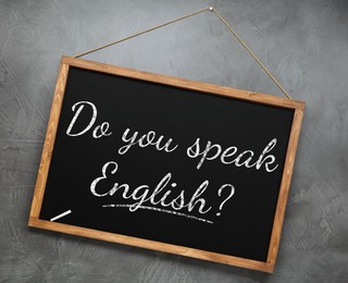 Image of Small black chalkboard with text Do You Speak English? on grey background. Language course