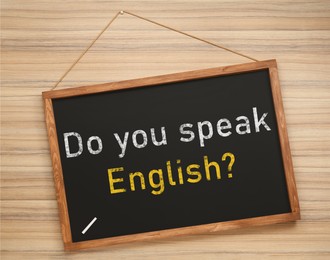 Small black chalkboard with text Do You Speak English? on wooden background. Language course