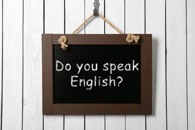 Image of Small black chalkboard with text Do You Speak English? on white wooden wall. Language course