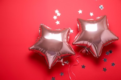 Photo of Star shaped pink balloons and confetti on red background, flat lay