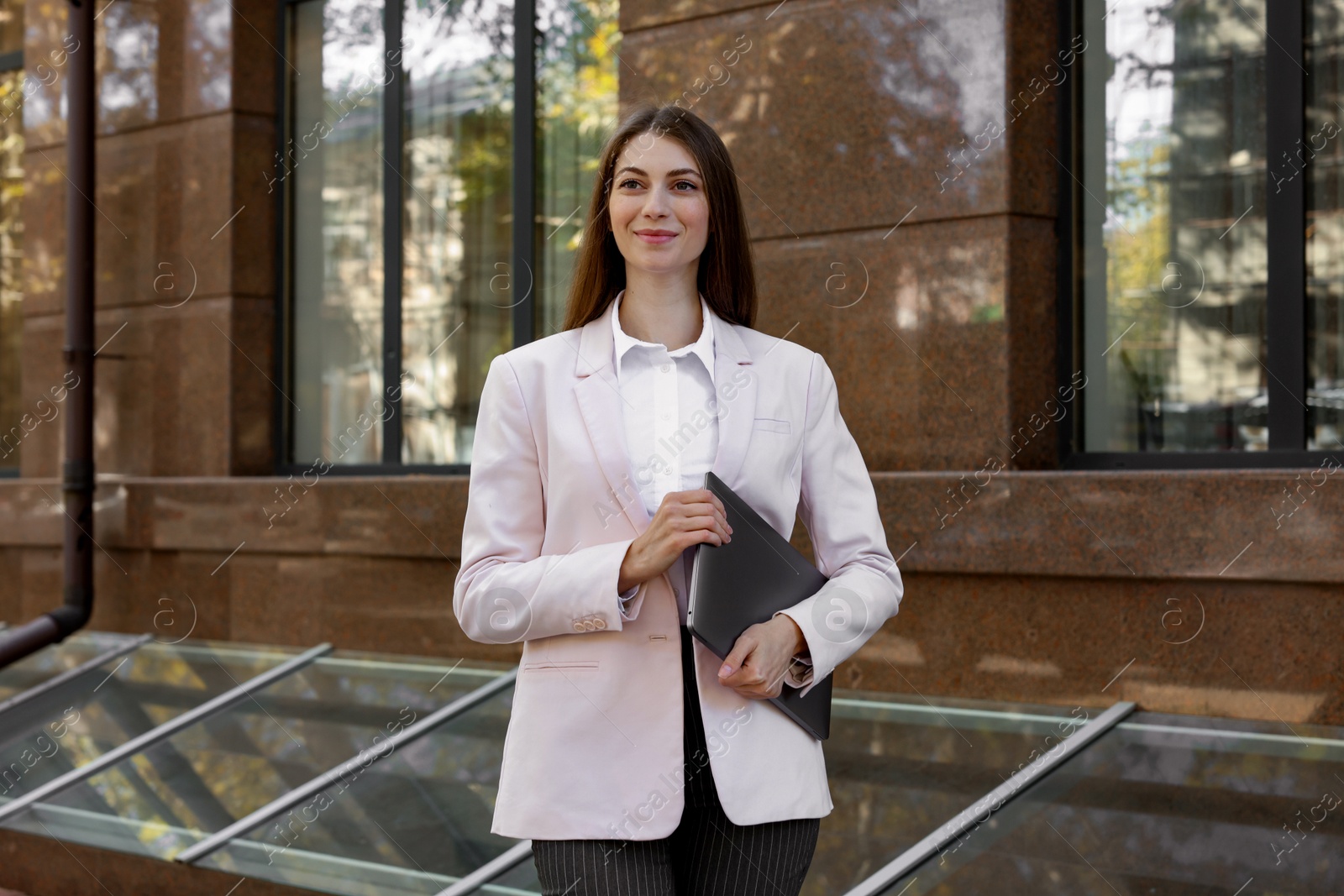 Photo of Portrait of young woman with laptop wearing stylish suit outdoors