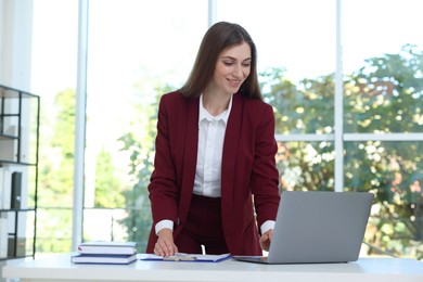 Portrait of young woman with laptop wearing stylish suit at white table indoors